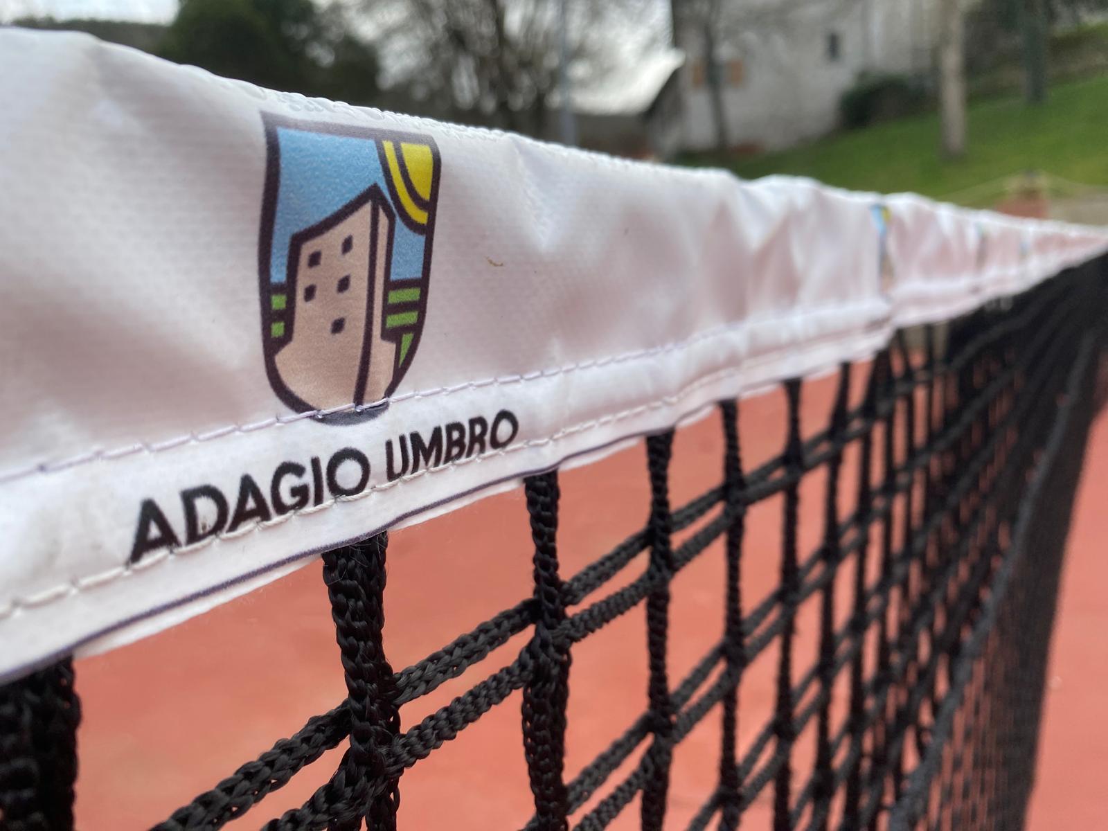 Tennis net with Adagio Umbro logo, set against the scenic backdrop of the tennis court in Umbria, Italy.